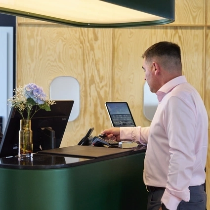 Customer at a hotel reception desk using a payment terminal while interacting with a staff member across the counter