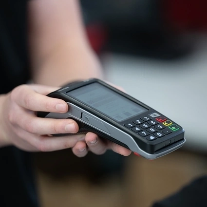 Person holding a payment terminal, preparing to process a card payment for a customer